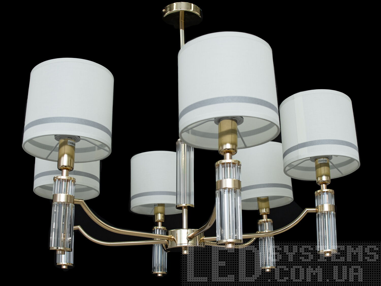 Люстра на 6 ламп у залу в класичному стилі з абажурами з витонченою металевою основою та стильними кришталевими елементами. Ви можете вибирати виконання металевих частин у золотому або хромованому варіанті. Застосовується для вітальні, залу, холу, спальні. У цій серії люстр і бра ідеально переплелися такі поняття, як солідність, строгість і простота.
Люстри та бра цієї моделі під звичайні лампи розжарювання або &laquo;LED-економки&raquo; на патрон Е14 внесуть класичні нотки до Вашого інтер'єру та дозволять підібрати потрібну вам температуру світіння.Універсальним кріпленням на планку легко кріпляться на будь-який тип стелі (підвісний, натяжний, звичайний). Увімкнення/вимкнення відбувається з настінного вимикача.