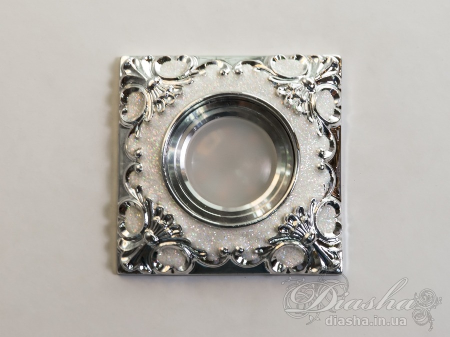 Гіпсовий точковий світильник є апофеозом класичного стилю та витонченої естетики. Він не просто виконує свою безпосередню функцію освітлення, але й слугує декоративним елементом, який здатен прикрасити і доповнити найвишуканіший інтер'єр.
Виготовлені з гіпсу, точкові світильники ідеально вписуються в класичну архітектуру приміщення, додаючи їй відчуття розкоші та історичної цінності. Їх можна гармонійно комбінувати з багетами та розетками під люстру, створюючи враження цілісності та продуманості кожної деталі.
Завдяки своїй універсальності, у цих світильниках можна використовувати як галогенові, так і світлодіодні лампи, які можуть бути підключені до мережі в 12 або 220 вольт. Світлодіодні лампи, зокрема, є найбільш енергоефективним вибором з великим терміном служби та мінімальним енергоспоживанням, що робить їх ідеальним рішенням для сучасного дому. При використанні ламп напругою 12В важливо не забувати про необхідність трансформатора, що забезпечить безпеку та стабільність роботи освітлювального приладу.
Зовнішній вигляд світильника з гіпсу вражає своєю ретельною обробкою та декоративними деталями. Витончені рослинні мотиви та золоті акценти на білому фоні створюють ефект аристократичної розкоші, підкреслюючи статусність інтер'єру та його власників. Це виріб не лише освітлює, а й привносить в будинок атмосферу величі та вишуканості.