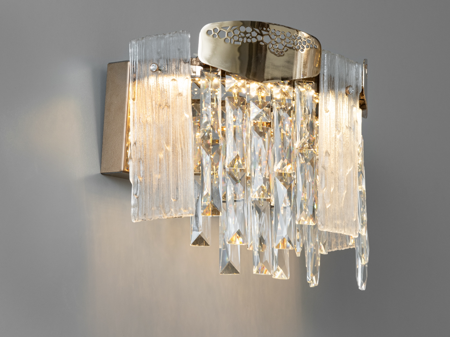 Елегантний настінний LED світильник у спальню є чимось більшим, ніж просто джерелом світла, він втілення мистецтва та елегантності. Застосовується в спальню, вітальню, коридор, а також для зали.
Металеві основи світильника пофарбовані в теплі відтінки золота і прикрашені візерунками, що нагадують мозаїку природного каміння, ретельно викладену руками майстра. Кожен кришталь створює неповторну гру світла.
Світлодіодний світильник має кілька режимів: холодний 6000К, нейтральний 4100К, теплий 3200К. Перемикання здійснюється з настінного вимикача почерговим включенням/вимкненням. Світлодіоди дозволяють підбирати необхідну температуру світла. Використання гнучкого світлодіодного модуля в люстрі дозволяє вивести естетичні якості на новий сучасний рівень.
Кріпиться до стін будь-якого типу універсальним кріпленням на монтажну планку.