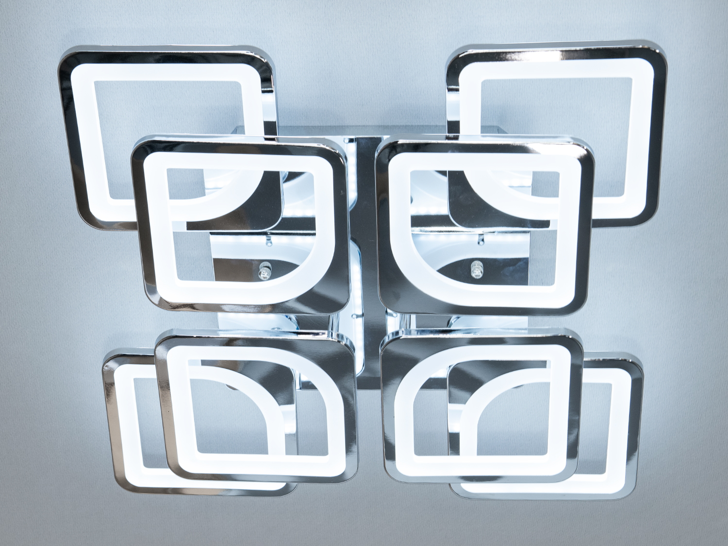 LED люстра у вітальню з димером – це поєднання мінімалізму та вишуканої геометрії. Її унікальна конструкція із восьми взаємоповязаних квадратів створює враження легкості та візуальної гармонії. Основа виконана з металу з гладкою хромованою або золотистою поверхнею, що додає виробу розкоші.