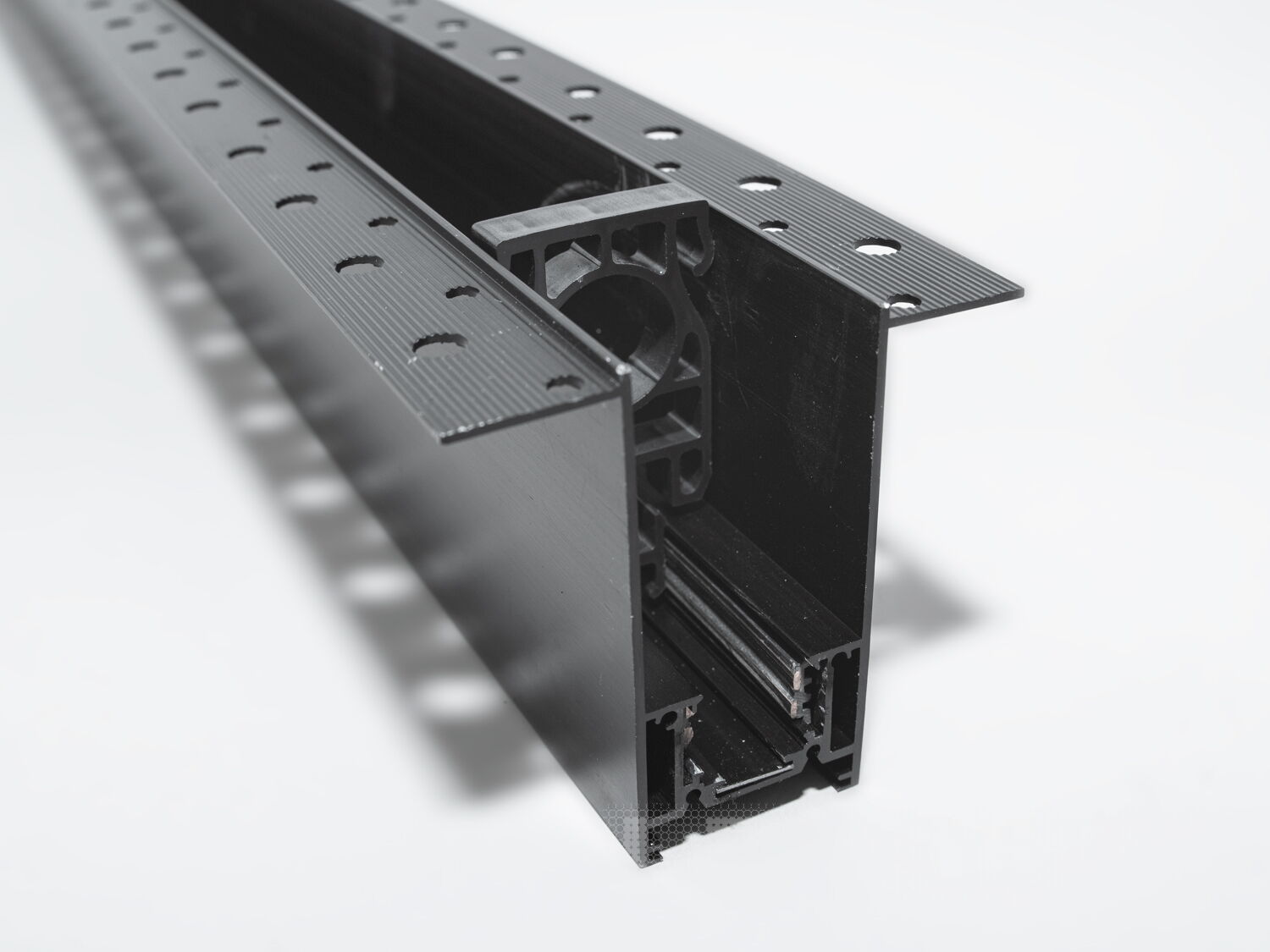 Рейлінг-шинопровід для магнітної трекової системи, розроблений для прихованої установки, є сучасним і технологічно вдосконаленим рішенням для створення гнучких освітлювальних сценаріїв. Ця система освітлення, що ледь помітна на стелі або стіні, ідеально підходить для тих, хто прагне до мінімалістичного та витонченого дизайну.
Шинопровід являє собою металевий профіль, який монтується врівень із поверхнею стелі або стіни, зазвичай перед покриттям гіпсокартоном або іншими оздоблювальними матеріалами. Він може бути встановлений між стельовими балками або на спеціальні монтажні планки, що забезпечують необхідну підтримку. Для монтажу цього треку достатньо штроби глибиною 85мм і шириною 45мм (у зовнішній частині 90 мм для фіксації шаром штукатурки закладних елементів). Після установки шинопроводу, поверхня стелі обробляється таким чином, що лише декоративна частина освітлювальних приладів залишається видимою.
Всередині шинопроводу проходять електричні проводи, які забезпечують живлення світильників. Магнітні компоненти в шинопроводі дозволяють легко прикріплювати або переміщувати світильники, тим самим, надаючи можливість змінювати освітлення відповідно до поточних потреб або перепланування простору.
Шинопровід складається із двох пар провідників. Одна пара для живлення світильників. Друга резервна для підключення управління світильниками, наприклад, за допомогою контролерів стандарту DALI.
Шинопровід розрахований на використання напруги живлення 48В. У конструкції використані шини прямокутного перерізу, які забезпечують більшу площу перерізу провідника, та кращий контакт, ніж шини з круглим перетином.
Додатковою перевагою є те, що така прихована система дозволяє уникнути видимого нагромадження технічних елементів на стелі, зберігаючи естетичну чистоту дизайну. Це створює ілюзію, що світло виходить прямо з поверхні, додаючи відчуття простору і візуально розширюючи кімнату.
Рейлінг-шинопровід для прихованої установки може мати різні форми і розміри, що надає додаткової гнучкості при проектуванні освітлювальних рішень. Він також може бути пофарбований у колір стелі, щоб ще більше інтегруватися в інтер'єр.
Завдяки використанню стандартного профілю для системи 48В, можна комбінувати треки та світильники різних виробників в одній системі.
Такі системи часто застосовуються в комерційних і житлових просторах, які підкреслюють сучасний дизайн інтер'єру, де освітлення є ключовим елементом декору. Вони забезпечують не тільки функціональне освітлення, а й виконують роль декоративного елементу, додаючи інтер'єру завершеності та стилю.