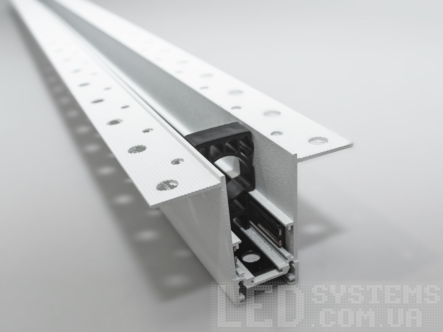 Рейлінг-шинопровід для магнітної трекової системи, розроблений для прихованої установки, є сучасним і технологічно вдосконаленим рішенням для створення гнучких освітлювальних сценаріїв. Ця система освітлення, що ледь помітна на стелі або стіні, ідеально підходить для тих, хто прагне до мінімалістичного та витонченого дизайну.
Шинопровід являє собою металевий профіль, який монтується врівень із поверхнею стелі або стіни, зазвичай перед покриттям гіпсокартоном або іншими оздоблювальними матеріалами. Він може бути встановлений між стельовими балками або на спеціальні монтажні планки, що забезпечують необхідну підтримку. Для монтажу цього треку достатньо штроби глибиною 85мм і шириною 45мм (у зовнішній частині 90 мм для фіксації шаром штукатурки закладних елементів). Після установки шинопроводу, поверхня стелі обробляється таким чином, що лише декоративна частина освітлювальних приладів залишається видимою.
Всередині шинопроводу проходять електричні проводи, які забезпечують живлення світильників. Магнітні компоненти в шинопроводі дозволяють легко прикріплювати або переміщувати світильники, тим самим, надаючи можливість змінювати освітлення відповідно до поточних потреб або перепланування простору.
Шинопровід складається із двох пар провідників. Одна пара для живлення світильників. Друга резервна для підключення управління світильниками, наприклад, за допомогою контролерів стандарту DALI.
Шинопровід розрахований на використання напруги живлення 48В. У конструкції використані шини прямокутного перерізу, які забезпечують більшу площу перерізу провідника, та кращий контакт, ніж шини з круглим перетином.
Додатковою перевагою є те, що така прихована система дозволяє уникнути видимого нагромадження технічних елементів на стелі, зберігаючи естетичну чистоту дизайну. Це створює ілюзію, що світло виходить прямо з поверхні, додаючи відчуття простору і візуально розширюючи кімнату.
Рейлінг-шинопровід для прихованої установки може мати різні форми і розміри, що надає додаткової гнучкості при проектуванні освітлювальних рішень. Він також може бути пофарбований у колір стелі, щоб ще більше інтегруватися в інтер'єр.
Завдяки використанню стандартного профілю для системи 48В, можна комбінувати треки та світильники різних виробників в одній системі.
Такі системи часто застосовуються в комерційних і житлових просторах, які підкреслюють сучасний дизайн інтер'єру, де освітлення є ключовим елементом декору. Вони забезпечують не тільки функціональне освітлення, а й виконують роль декоративного елементу, додаючи інтер'єру завершеності та стилю.