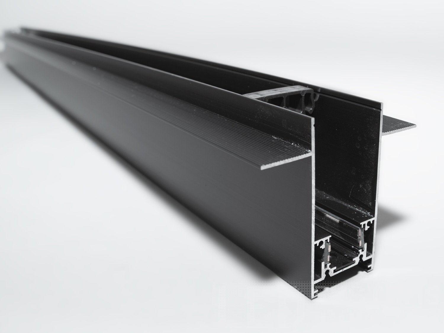 Рейлінг-шинопровід для магнітної трекової системи, спеціально розроблений для встановлення в гіпсокартон, є інноваційним рішенням для створення вишуканих та функціональних освітлювальних схем в сучасних інтер'єрах. Цей тип шинопроводу ідеально підходить для інтеграції в гіпсокартонні стелі або стіни, дозволяючи світильникам здаватися, ніби вони виникають із самої поверхні, забезпечуючи чистий і неперервний вигляд.
Конструкція такого шинопроводу включає монтажну основу, яка встановлюється на металевий каркас гіпсокартонної конструкції перед фінішною обробкою. Після монтажу основи та підключення електричних компонентів, гіпсокартонні панелі монтується навколо шинопроводу, приховуючи всі монтажні елементи. Світлодіодні світильники або інші освітлювальні прилади потім можуть бути прикріплені до магнітної шини, що залишається доступною через вирізи в гіпсокартоні.
Для забезпечення безпеки та тривалої служби такого шинопроводу, важливо забезпечити правильний монтаж та використання матеріалів, які відповідають всім необхідним будівельним стандартам та нормам. Це включає в себе не тільки сам шинопровід, але і всі супутні електричні з'єднання та ізоляцію.
Шинопровід для гіпсокартону може мати різні конфігурації, щоб відповідати різноманітним дизайнерським вимогам, наприклад, бути прямим, кутовим або навіть гнучким для створення криволінійних форм. Така гнучкість у дизайні відкриває необмежені можливості для творчості в освітленні інтер'єру, дозволяючи архітекторам та дизайнерам створювати унікальні та індивідуальні освітлювальні схеми.
Шинопровід складається із двох пар провідників. Одна пара для живлення світильників. Друга резервна, для підключення управління світильниками, наприклад, за допомогою контролерів стандарту DALI.
Шинопровід розрахований на використання напруги живлення 48В. У конструкції використані шини прямокутного перерізу, які забезпечують більшу площу перерізу провідника, та кращий контакт, ніж шини з круглим перетином.
Завдяки використанню стандартного профілю для системи 48В, можна комбінувати треки та світильники різних виробників в одній системі.
Окрім естетичних переваг, рейлінг-шинопровід для гіпсокартону дозволяє легко обслуговувати та замінювати світлові елементи без необхідності вносити зміни в саму конструкцію стелі або стіни, що робить його практичним вибором для комерційних та житлових приміщень.