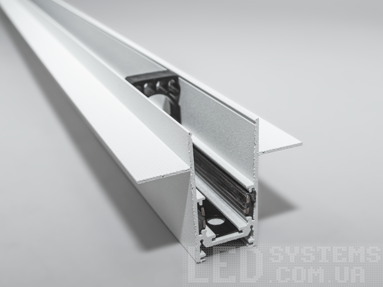 Рейлінг-шинопровід для магнітної трекової системи, спеціально розроблений для встановлення в гіпсокартон, є інноваційним рішенням для створення вишуканих та функціональних освітлювальних схем в сучасних інтер'єрах. Цей тип шинопроводу ідеально підходить для інтеграції в гіпсокартонні стелі або стіни, дозволяючи світильникам здаватися, ніби вони виникають із самої поверхні, забезпечуючи чистий і неперервний вигляд.
Конструкція такого шинопроводу включає монтажну основу, яка встановлюється на металевий каркас гіпсокартонної конструкції перед фінішною обробкою. Після монтажу основи та підключення електричних компонентів, гіпсокартонні панелі монтується навколо шинопроводу, приховуючи всі монтажні елементи. Світлодіодні світильники або інші освітлювальні прилади потім можуть бути прикріплені до магнітної шини, що залишається доступною через вирізи в гіпсокартоні.
Для забезпечення безпеки та тривалої служби такого шинопроводу, важливо забезпечити правильний монтаж та використання матеріалів, які відповідають всім необхідним будівельним стандартам та нормам. Це включає в себе не тільки сам шинопровід, але і всі супутні електричні з'єднання та ізоляцію.
Шинопровід для гіпсокартону може мати різні конфігурації, щоб відповідати різноманітним дизайнерським вимогам, наприклад, бути прямим, кутовим або навіть гнучким для створення криволінійних форм. Така гнучкість у дизайні відкриває необмежені можливості для творчості в освітленні інтер'єру, дозволяючи архітекторам та дизайнерам створювати унікальні та індивідуальні освітлювальні схеми.
Шинопровід складається із двох пар провідників. Одна пара для живлення світильників. Друга резервна, для підключення управління світильниками, наприклад, за допомогою контролерів стандарту DALI.
Шинопровід розрахований на використання напруги живлення 48В. У конструкції використані шини прямокутного перерізу, які забезпечують більшу площу перерізу провідника, та кращий контакт, ніж шини з круглим перетином.
Завдяки використанню стандартного профілю для системи 48В, можна комбінувати треки та світильники різних виробників в одній системі.
Окрім естетичних переваг, рейлінг-шинопровід для гіпсокартону дозволяє легко обслуговувати та замінювати світлові елементи без необхідності вносити зміни в саму конструкцію стелі або стіни, що робить його практичним вибором для комерційних та житлових приміщень.