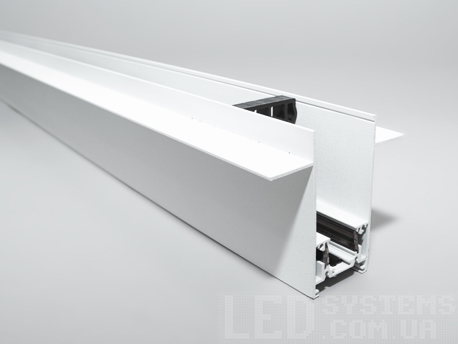 Рейлінг-шинопровід для магнітної трекової системи, спеціально розроблений для встановлення в гіпсокартон, є інноваційним рішенням для створення вишуканих та функціональних освітлювальних схем в сучасних інтер'єрах. Цей тип шинопроводу ідеально підходить для інтеграції в гіпсокартонні стелі або стіни, дозволяючи світильникам здаватися, ніби вони виникають із самої поверхні, забезпечуючи чистий і неперервний вигляд.
Конструкція такого шинопроводу включає монтажну основу, яка встановлюється на металевий каркас гіпсокартонної конструкції перед фінішною обробкою. Після монтажу основи та підключення електричних компонентів, гіпсокартонні панелі монтується навколо шинопроводу, приховуючи всі монтажні елементи. Світлодіодні світильники або інші освітлювальні прилади потім можуть бути прикріплені до магнітної шини, що залишається доступною через вирізи в гіпсокартоні.
Для забезпечення безпеки та тривалої служби такого шинопроводу, важливо забезпечити правильний монтаж та використання матеріалів, які відповідають всім необхідним будівельним стандартам та нормам. Це включає в себе не тільки сам шинопровід, але і всі супутні електричні з'єднання та ізоляцію.
Шинопровід для гіпсокартону може мати різні конфігурації, щоб відповідати різноманітним дизайнерським вимогам, наприклад, бути прямим, кутовим або навіть гнучким для створення криволінійних форм. Така гнучкість у дизайні відкриває необмежені можливості для творчості в освітленні інтер'єру, дозволяючи архітекторам та дизайнерам створювати унікальні та індивідуальні освітлювальні схеми.
Шинопровід складається із двох пар провідників. Одна пара для живлення світильників. Друга резервна, для підключення управління світильниками, наприклад, за допомогою контролерів стандарту DALI.
Шинопровід розрахований на використання напруги живлення 48В. У конструкції використані шини прямокутного перерізу, які забезпечують більшу площу перерізу провідника, та кращий контакт, ніж шини з круглим перетином.
Завдяки використанню стандартного профілю для системи 48В, можна комбінувати треки та світильники різних виробників в одній системі.
Окрім естетичних переваг, рейлінг-шинопровід для гіпсокартону дозволяє легко обслуговувати та замінювати світлові елементи без необхідності вносити зміни в саму конструкцію стелі або стіни, що робить його практичним вибором для комерційних та житлових приміщень.